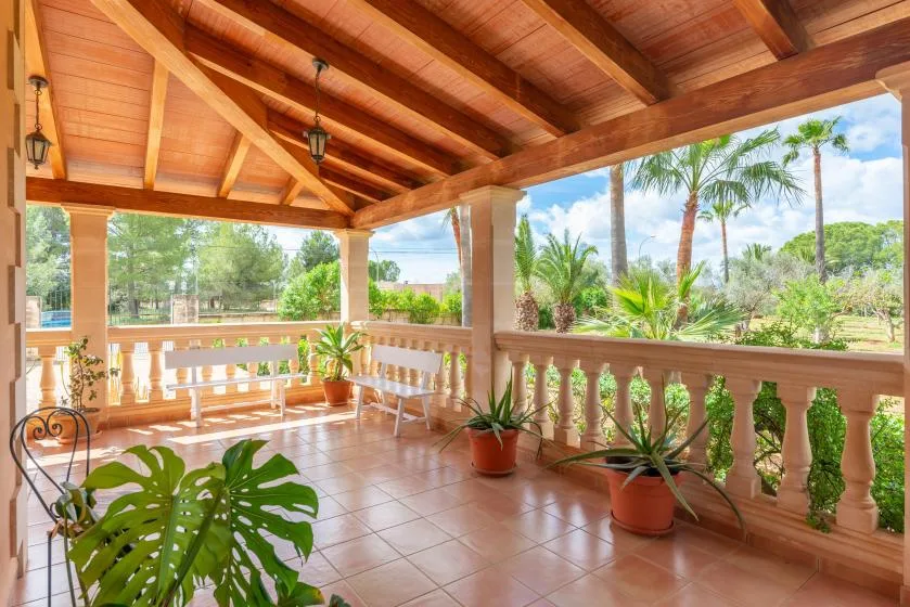 A covered patio with tiled flooring, wooden railings, and potted plants overlooks a garden.
