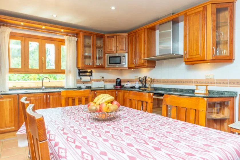 A bright kitchen with wooden cabinets and a dining table set with fruit.