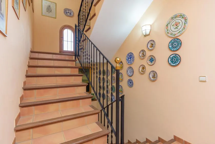 A tiled staircase with a dark railing and decorative plates on the wall.
