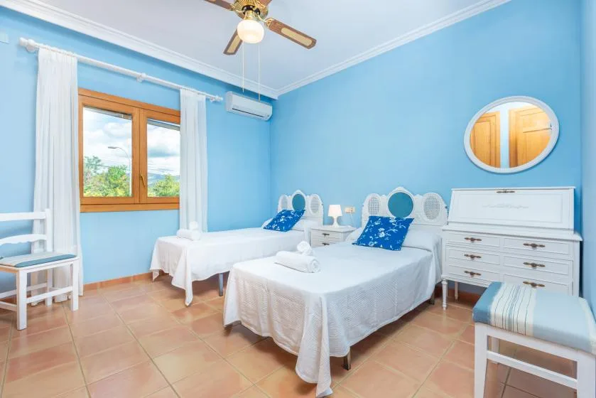 A blue bedroom with two beds and a window with white curtains.