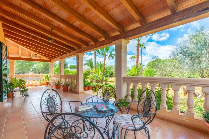 A covered terrace with a table and seating overlooks palm trees and greenery.