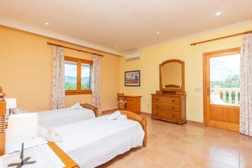 A bright bedroom with white bedding, wooden furniture, and a door opening onto a balcony.