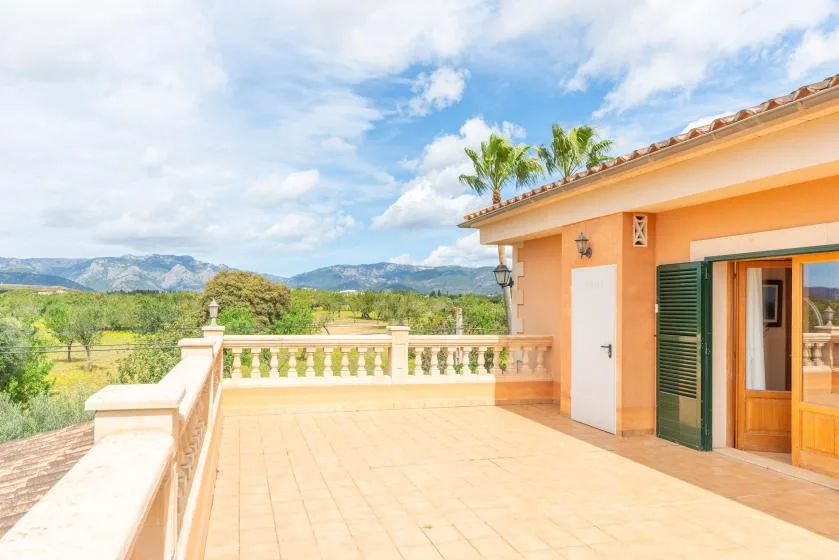 A sunny tiled terrace beside an orange house overlooks green hills.