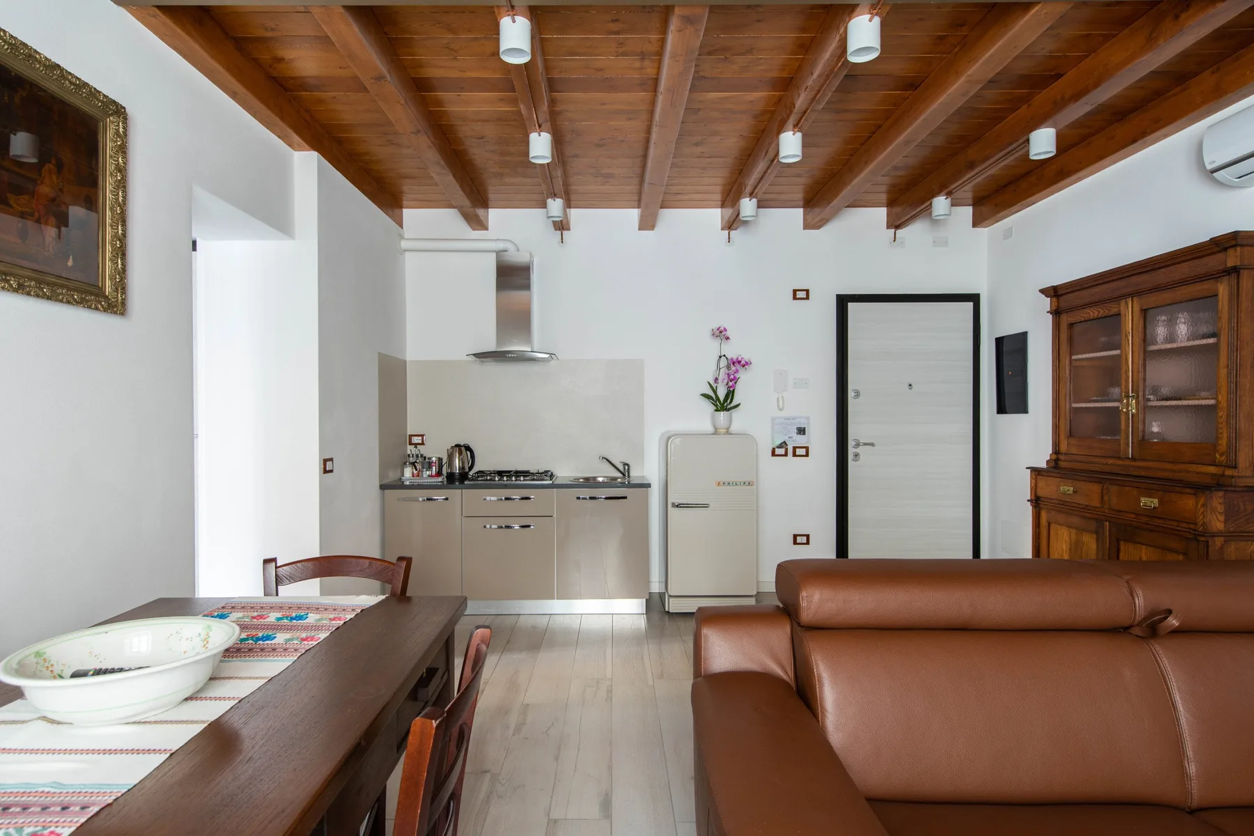 Una zona de estar y comedor con asientos marrones, una mesa de comedor y vigas de madera vistas en el techo.