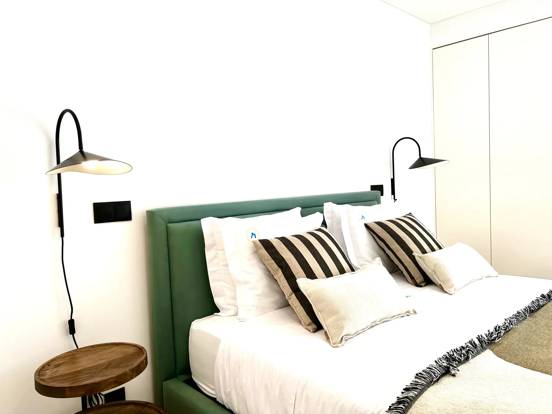 Dormitorio con una cama bien hecha, cabecero verde tapizado y lámparas de noche.