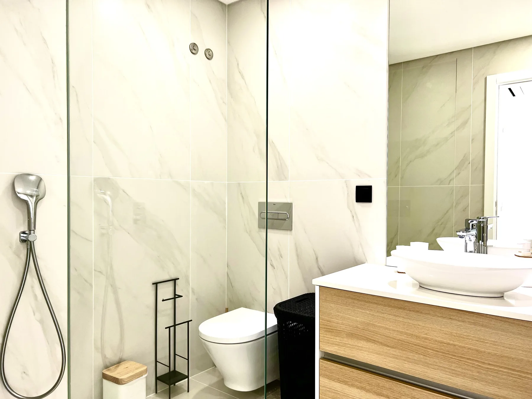 Un baño luminoso con ducha de vidrio, inodoro y lavabo con mueble de madera.