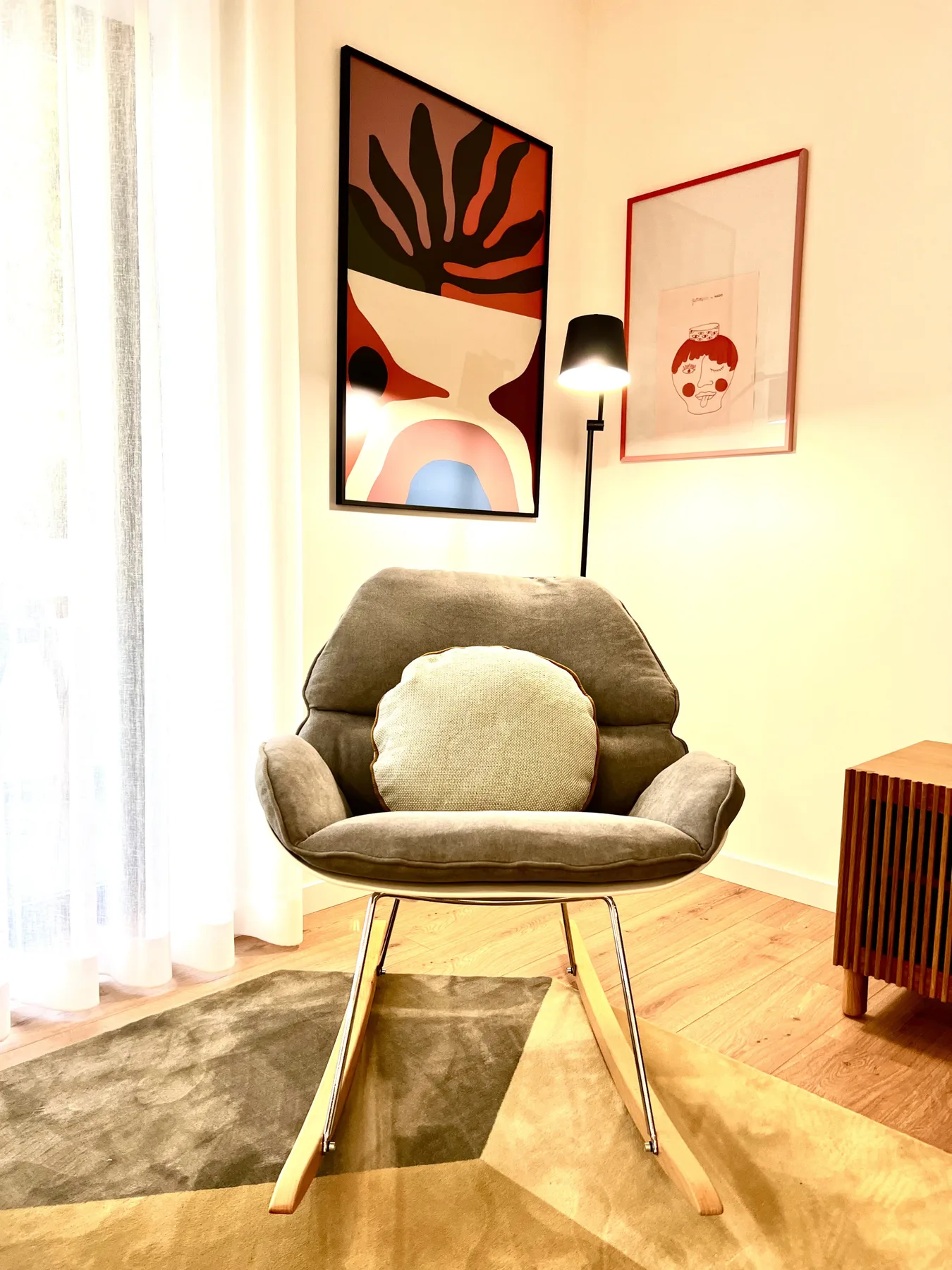 Una zona de estar con un sillón tapizado, una lámpara de pie y cuadros enmarcados.