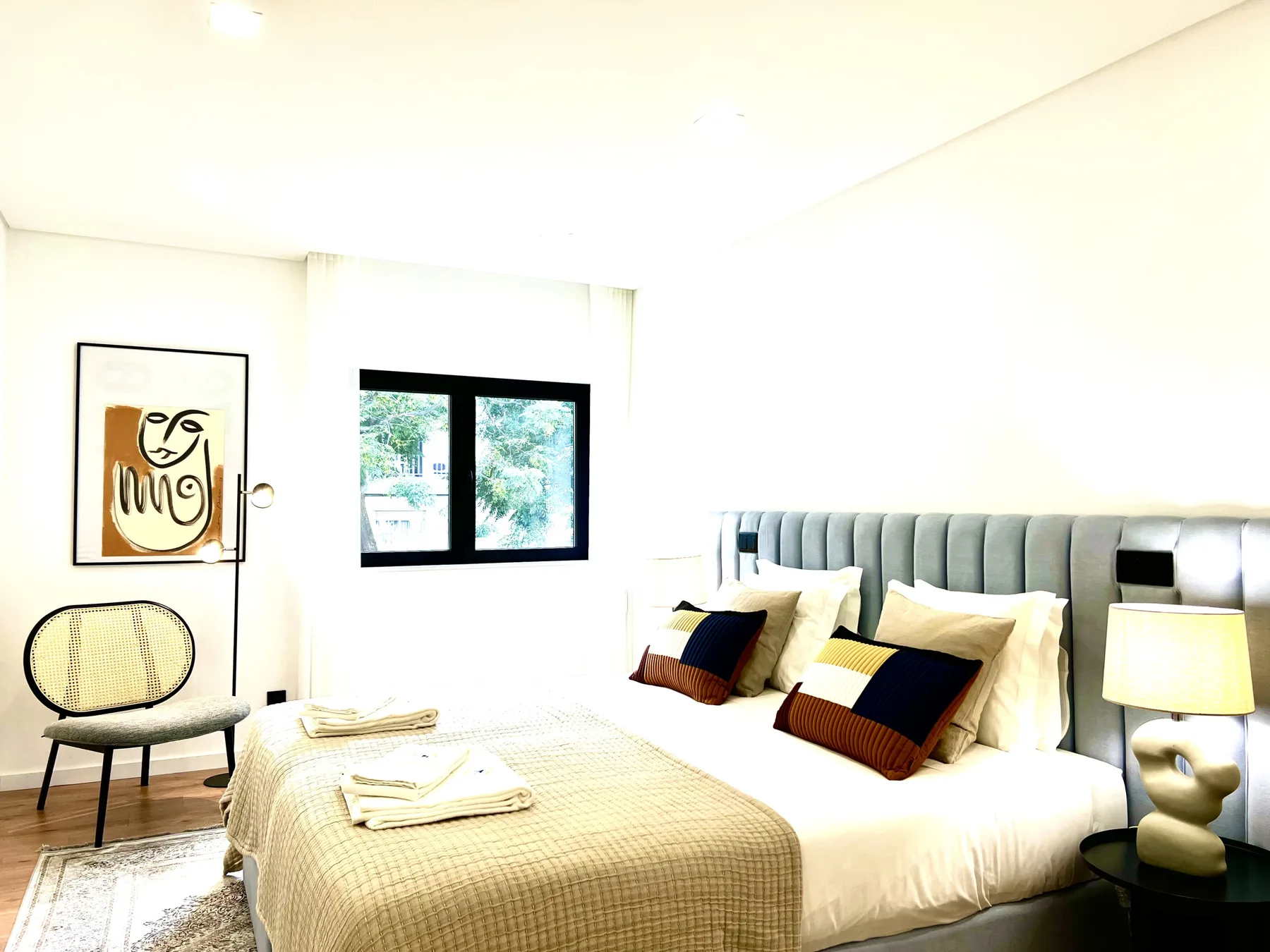 Dormitorio luminoso con una cama grande y una ventana con vistas a vegetación.