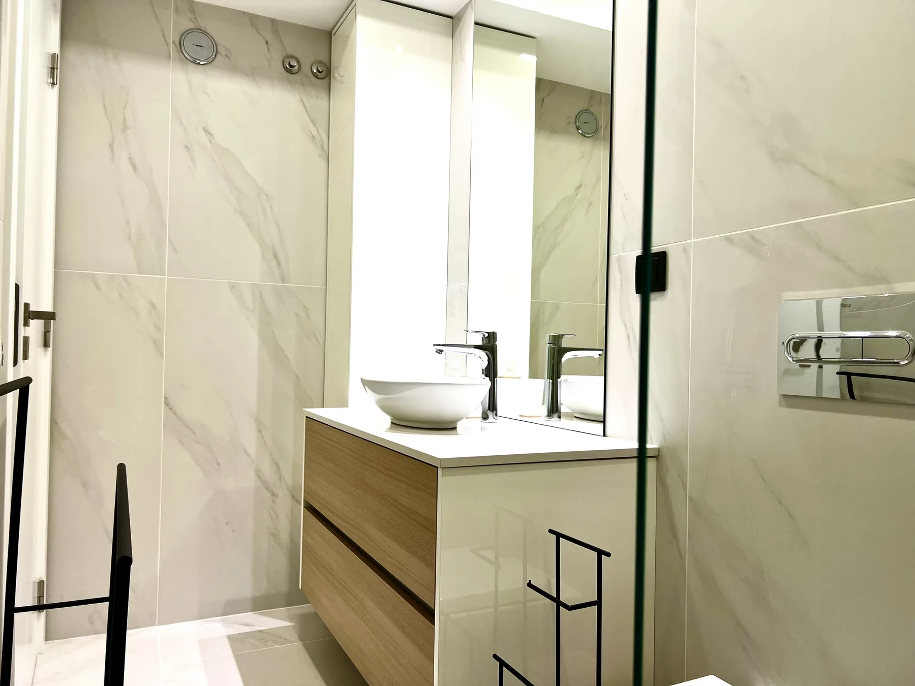 Un baño luminoso con ducha de vidrio, mueble de lavabo y accesorios en la pared.