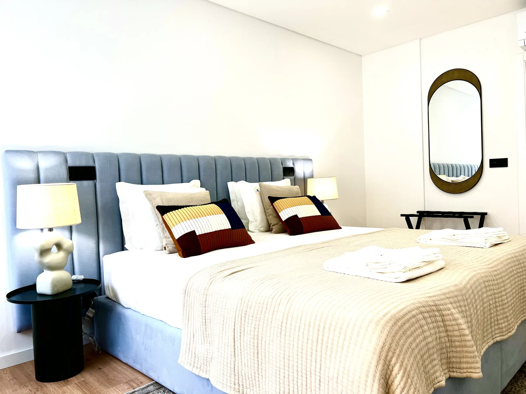 Un dormitorio luminoso con una cama, cabecero azul tapizado y lámpara de noche.