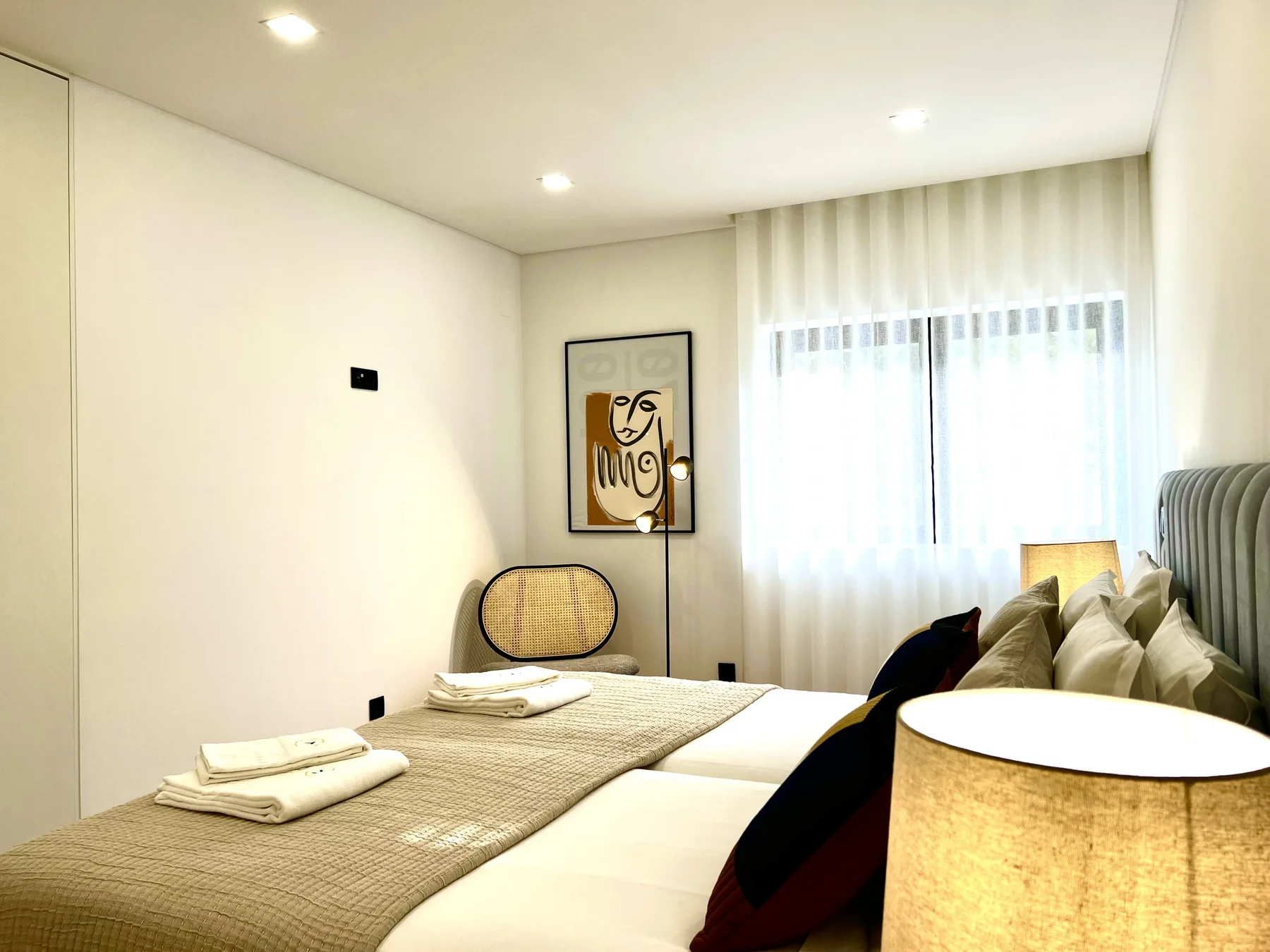 Un dormitorio luminoso con una cama bien tendida y una gran ventana con cortinas.