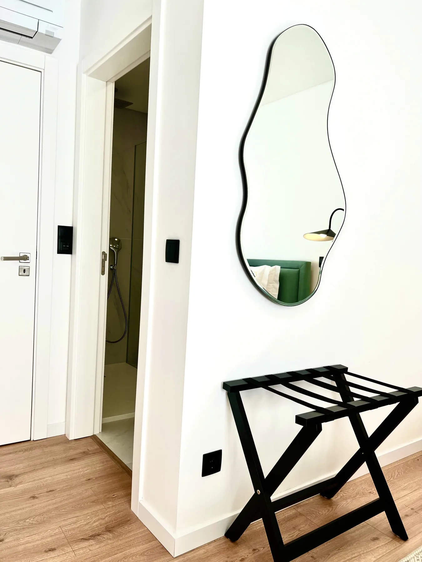 Un recibidor luminoso tiene una puerta abierta al baño y un espejo en la pared.