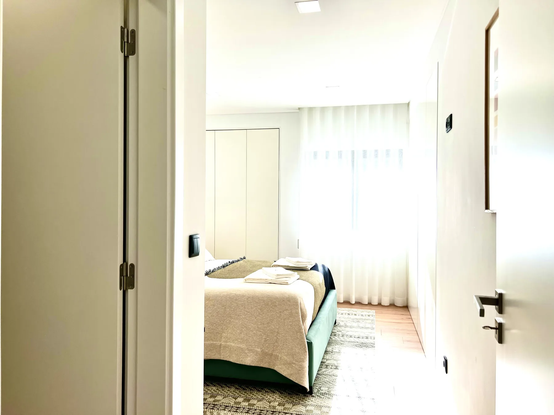Dormitorio luminoso con una cama junto a una gran ventana con cortinas.