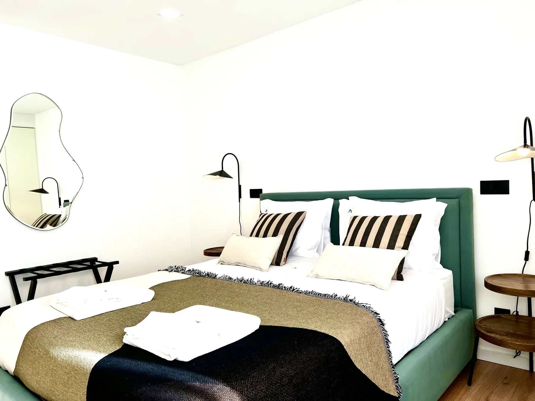 Un dormitorio con una cama verde, almohadas a rayas y lámparas de pared.