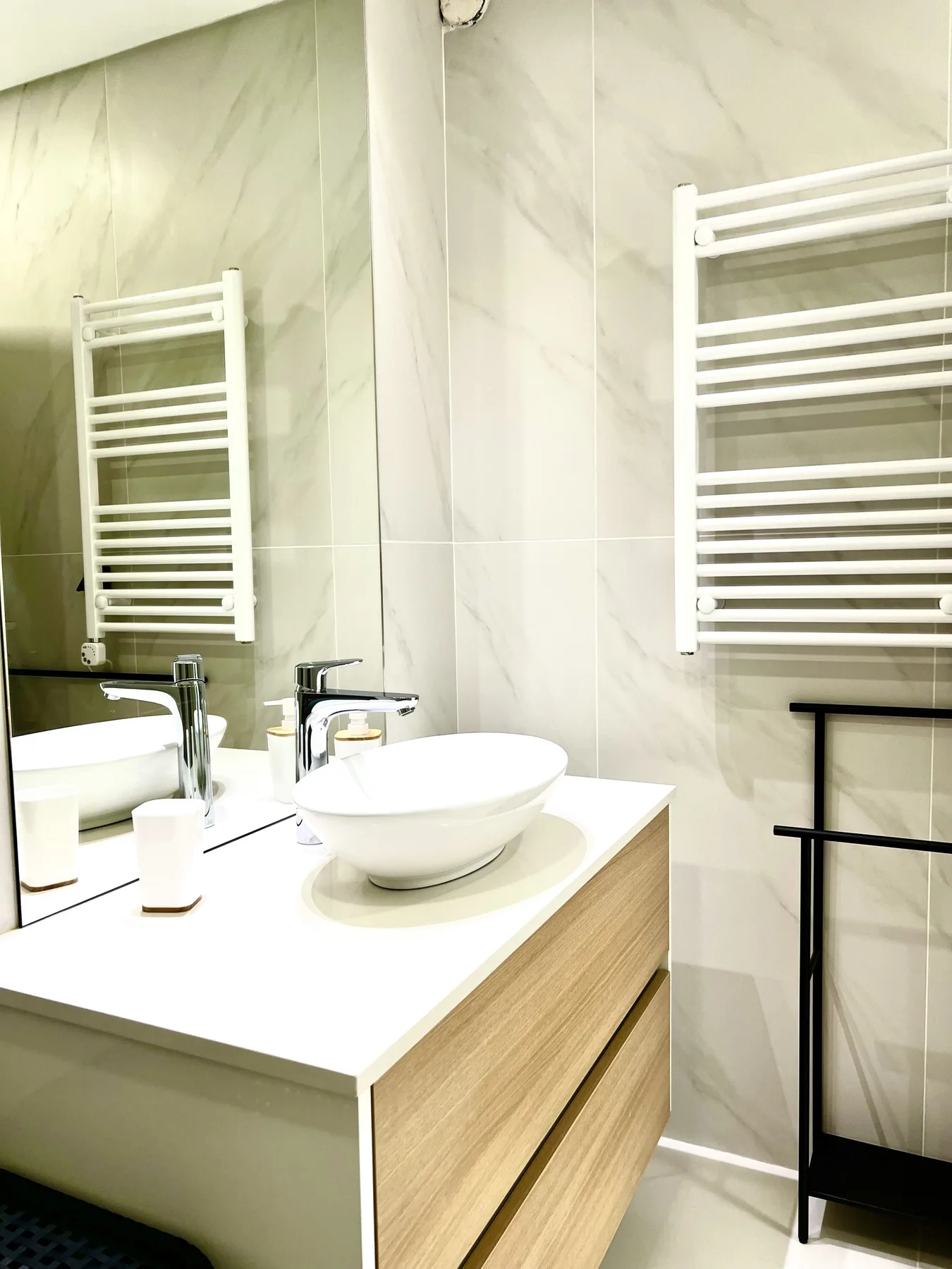 Un mueble de baño con lavabo sobre encimera, espejo y toallero calefactable.