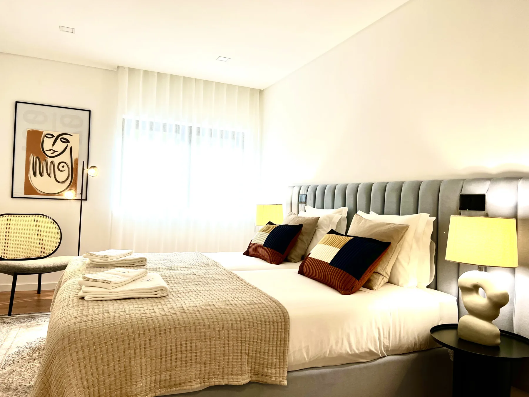 Un dormitorio luminoso con una cama bien tendida y una obra enmarcada.