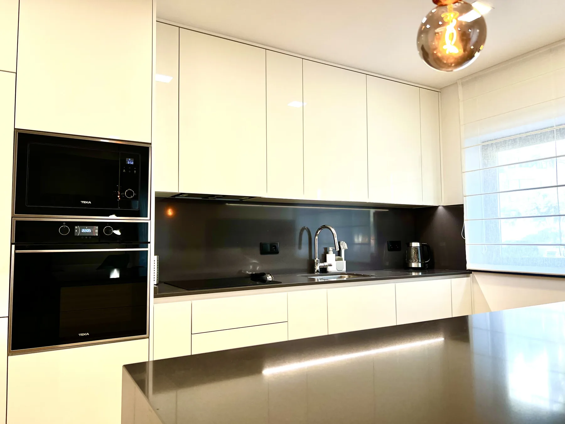Una cocina moderna con gabinetes blancos, encimeras oscuras y un fregadero.