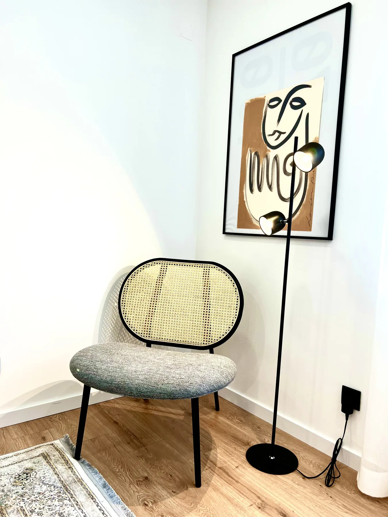 Una zona de estar con una silla de tejido, una lámpara de pie y una obra enmarcada.