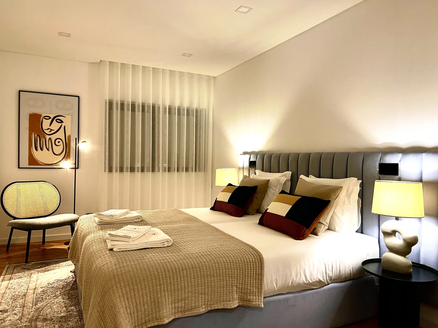 Un dormitorio con una cama bien tendida y cortinas translúcidas en la ventana.