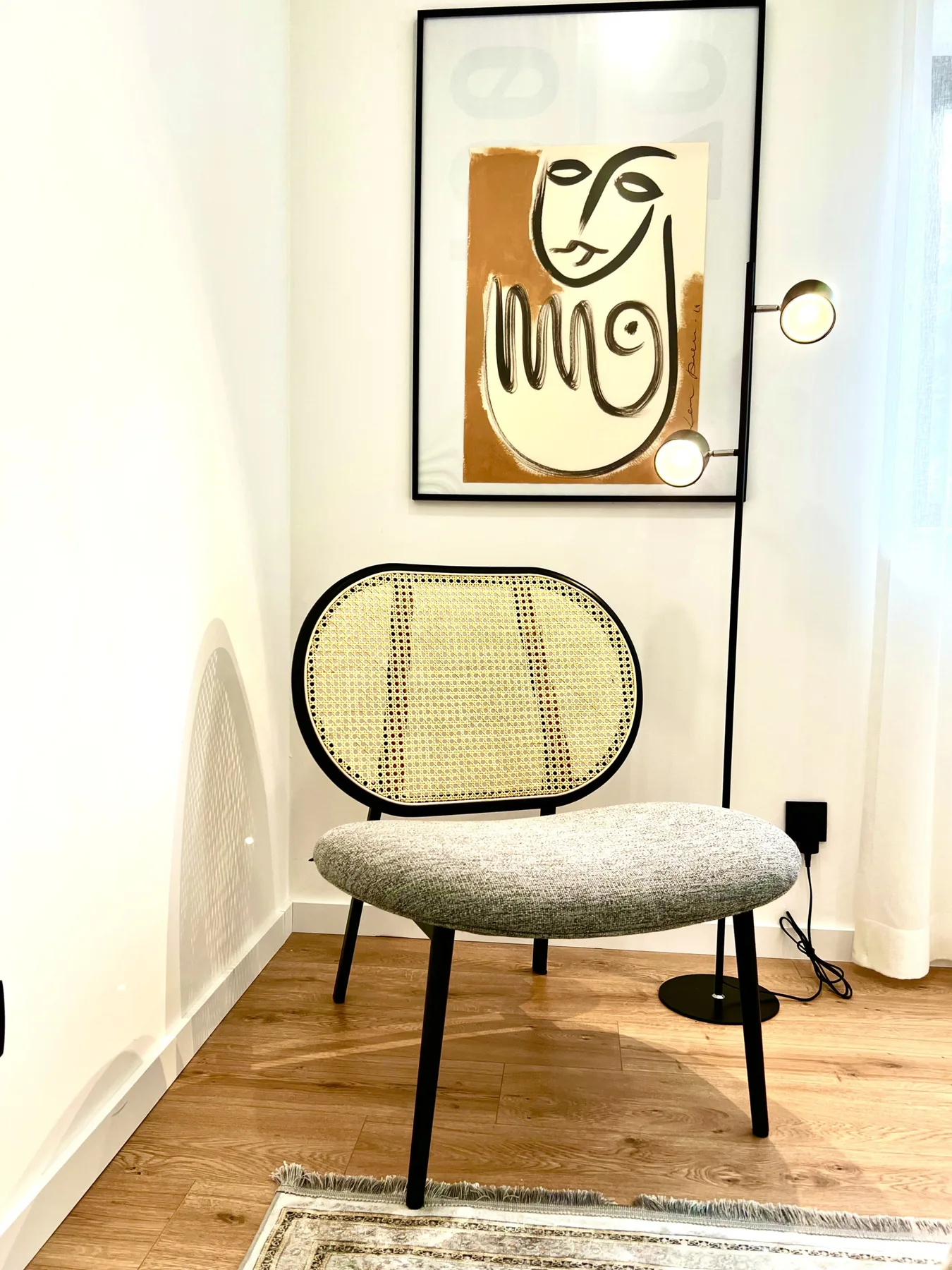 Un rincón moderno con una silla tejida bajo una obra de arte abstracta.