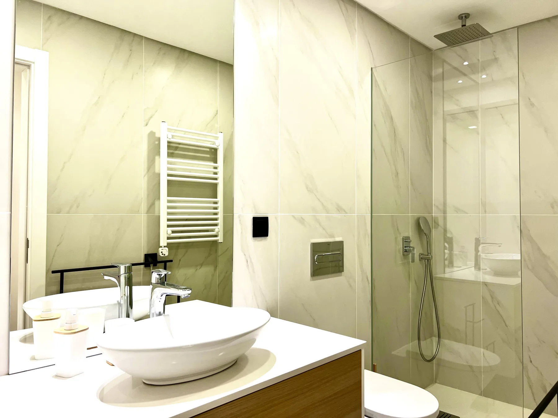 Un baño luminoso con azulejos, lavabo sobre encimera y ducha de vidrio.