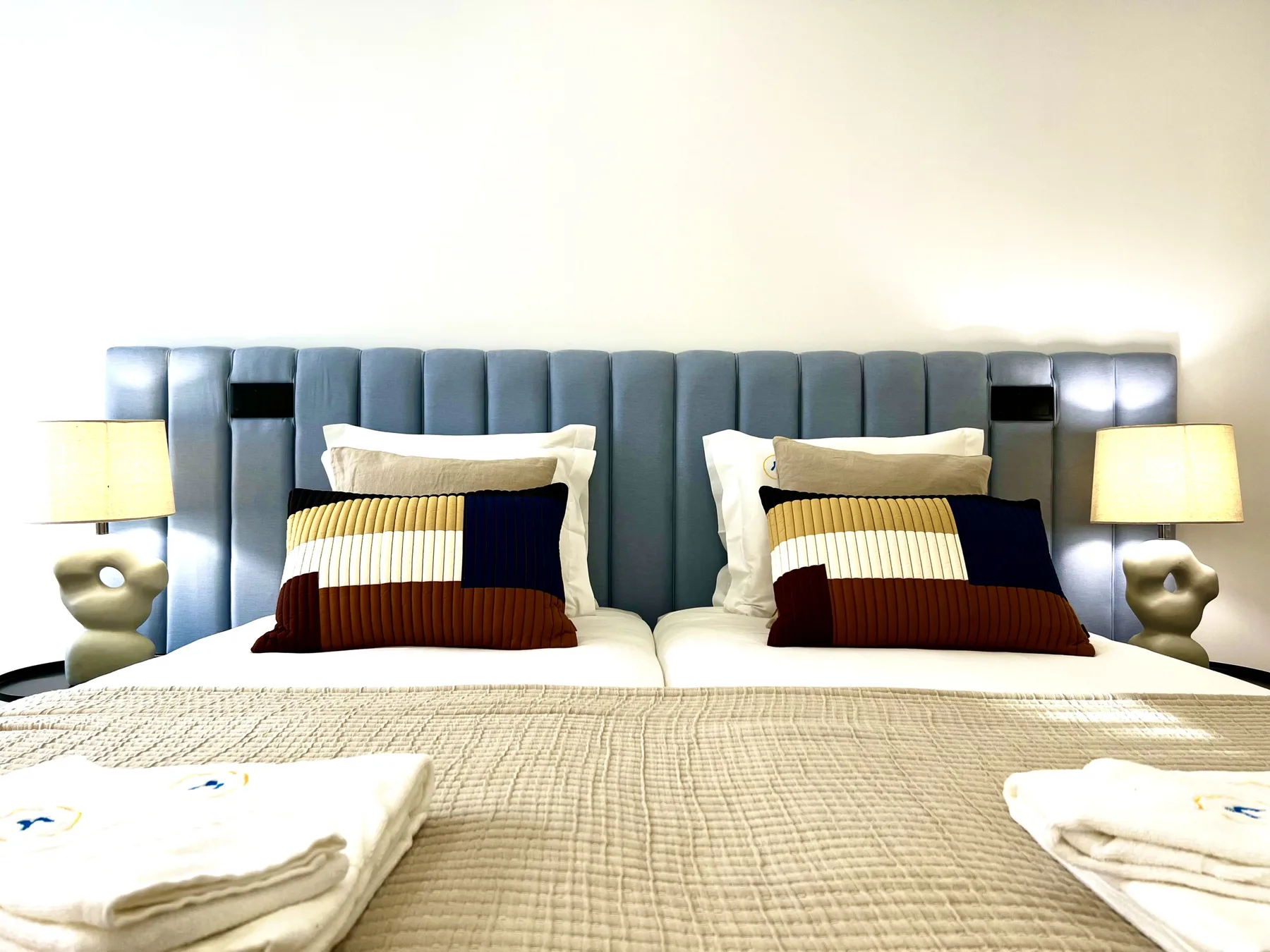 Un dormitorio con dos camas, almohadas superpuestas y lámparas a juego junto a ellas.