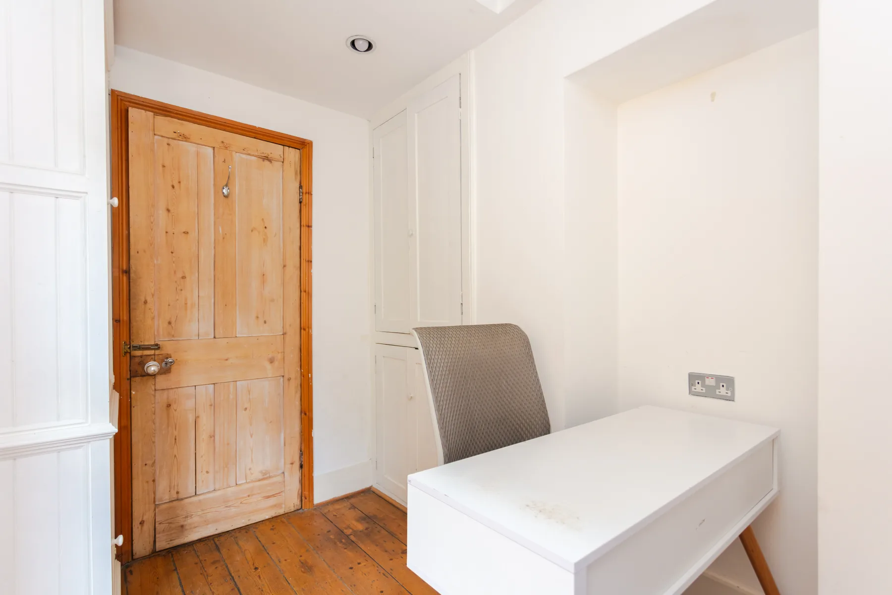 A bright room with a wooden door, a desk, and a chair.
