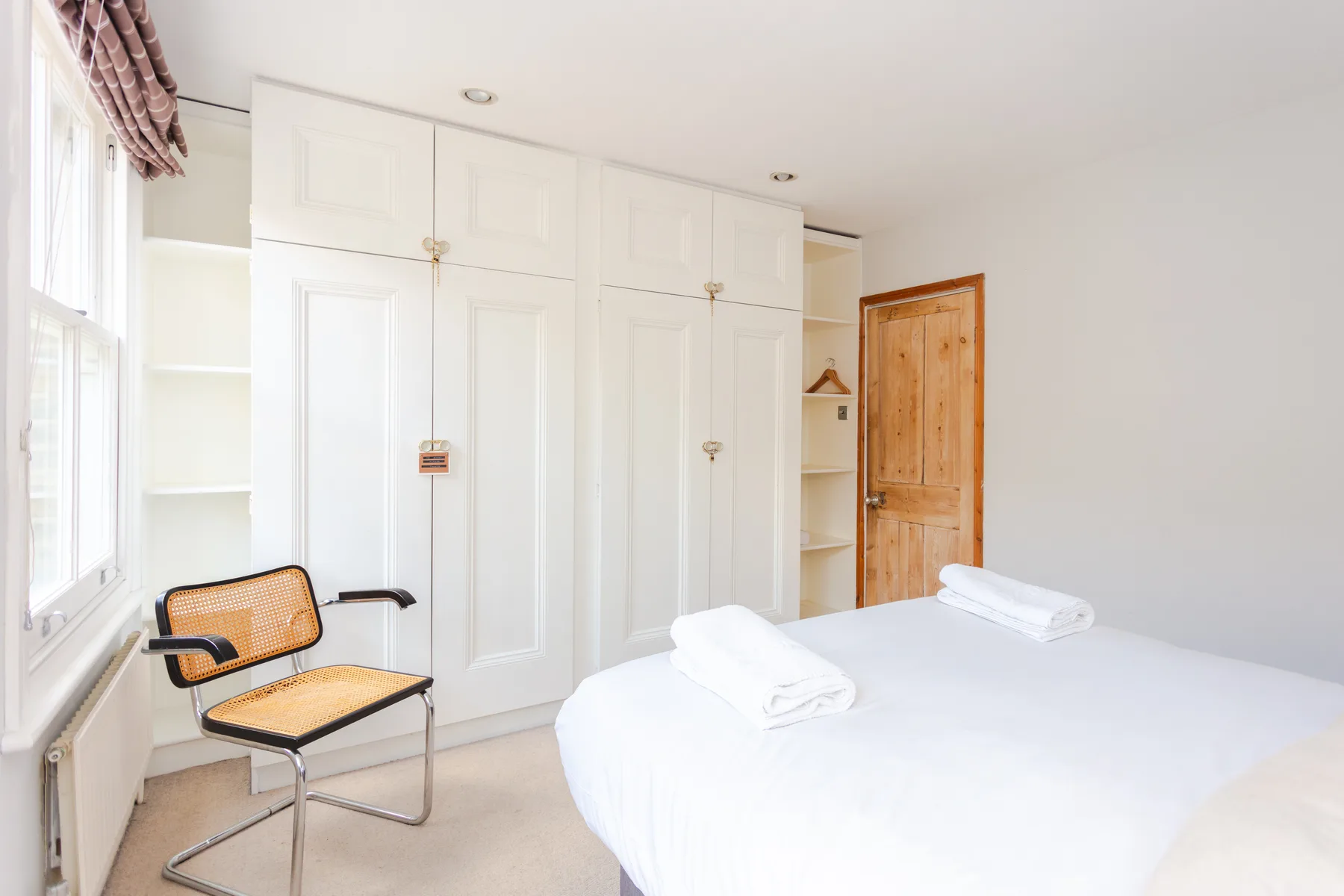 A bright bedroom with a neatly made bed and built-in cupboards.