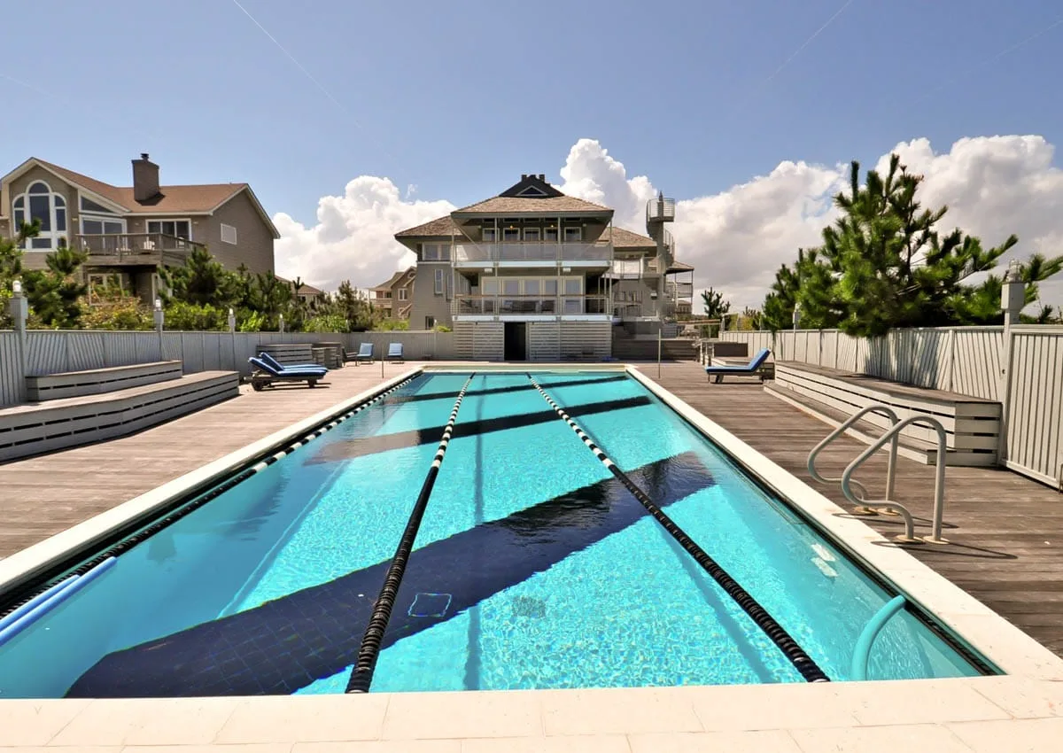 An outdoor swimming pool with lane markings is surrounded by a wooden deck.