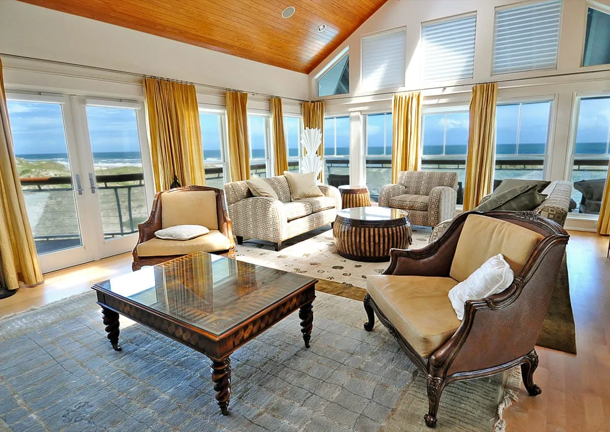 A bright living room with seating around a coffee table and windows overlooking the water.