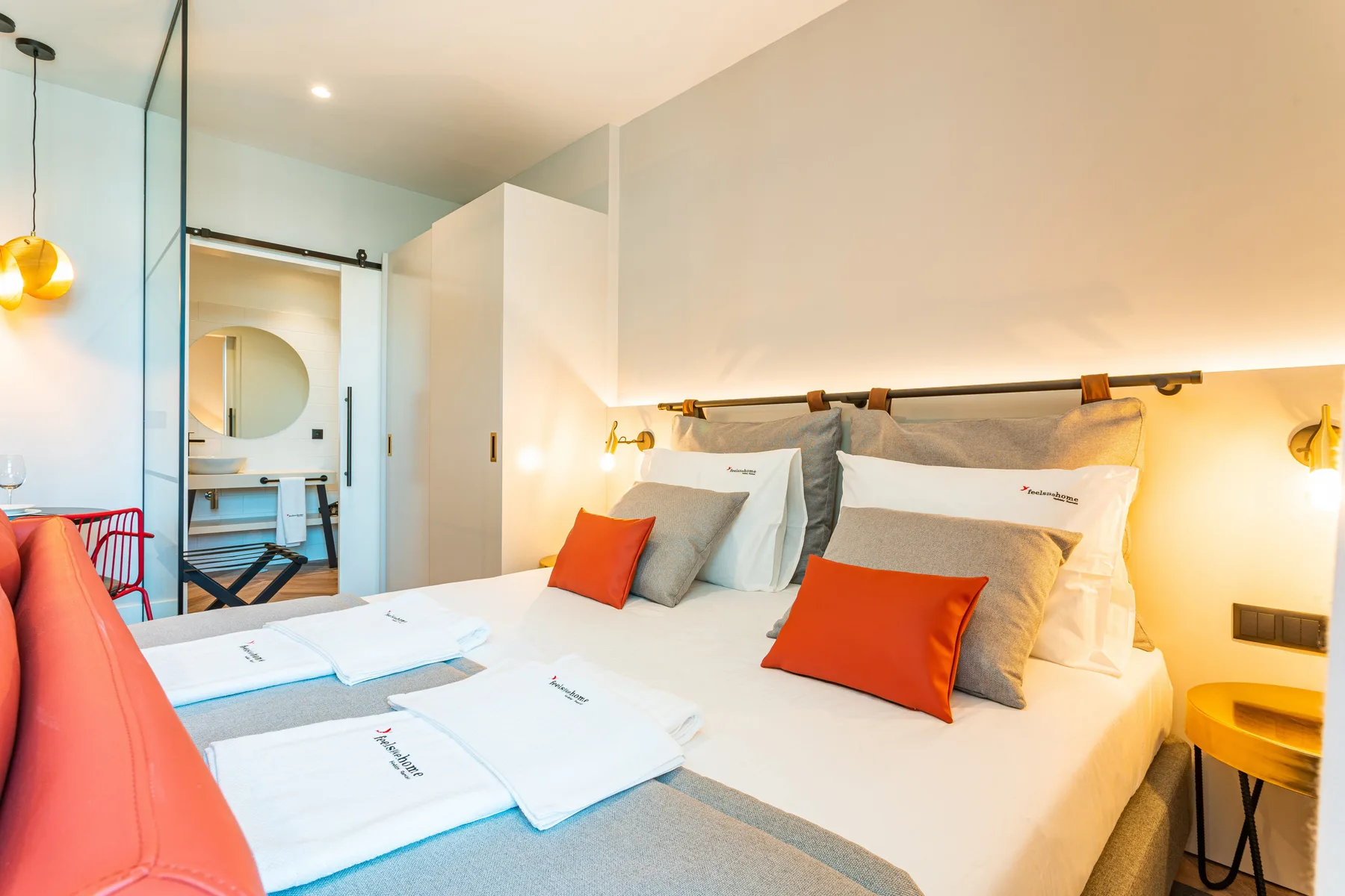 A bedroom with a neatly made bed and bright orange accent pillows.