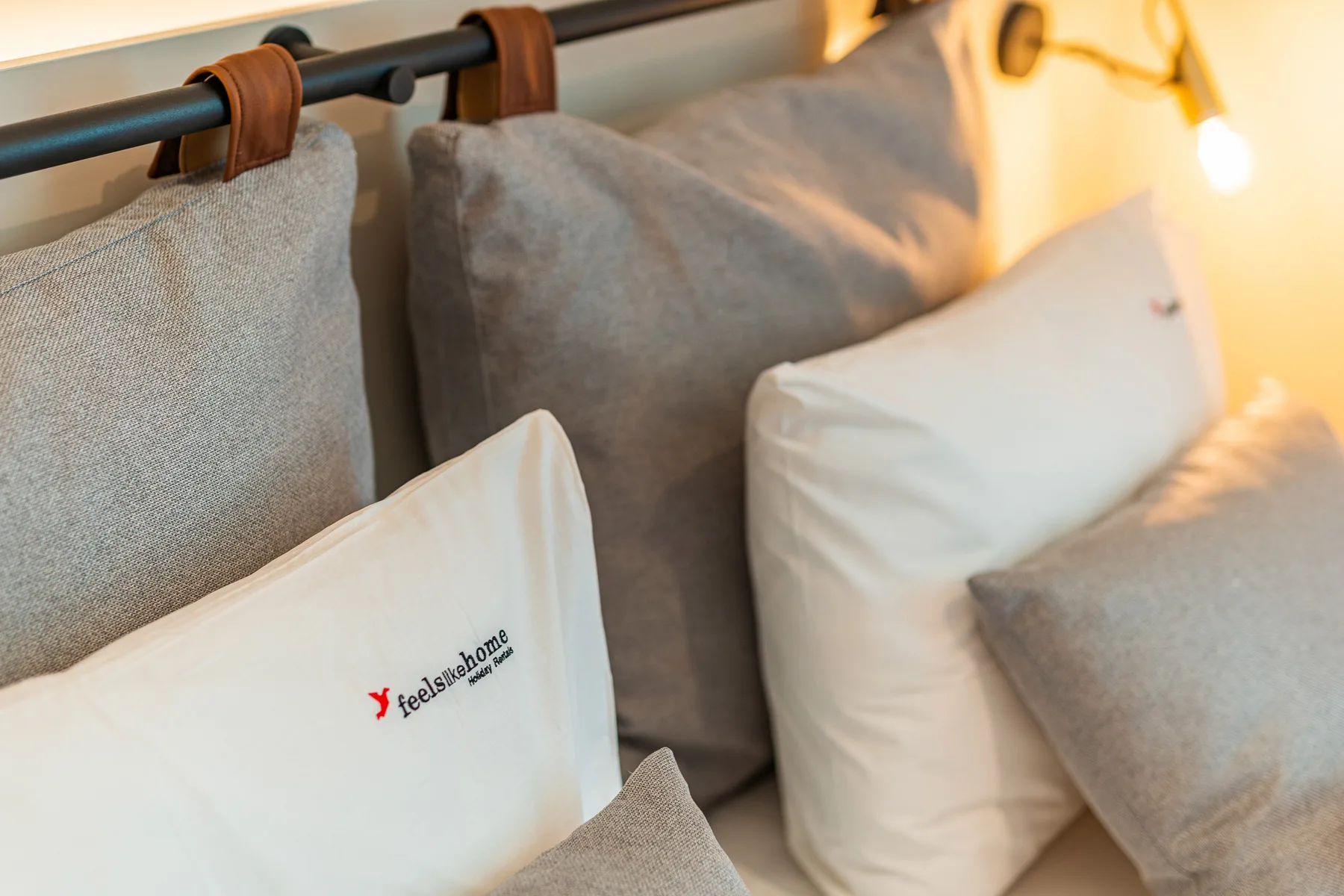 A bedroom scene with several pillows arranged along a dark headboard.