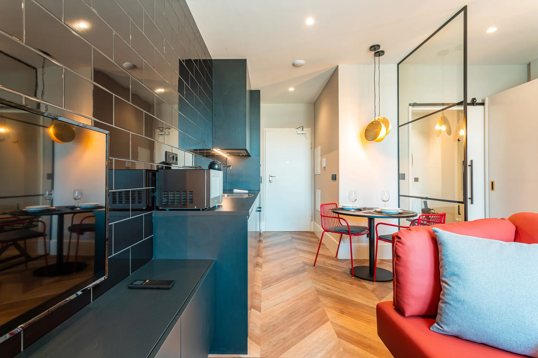 A studio interior combines a kitchen, dining area, and red seating.