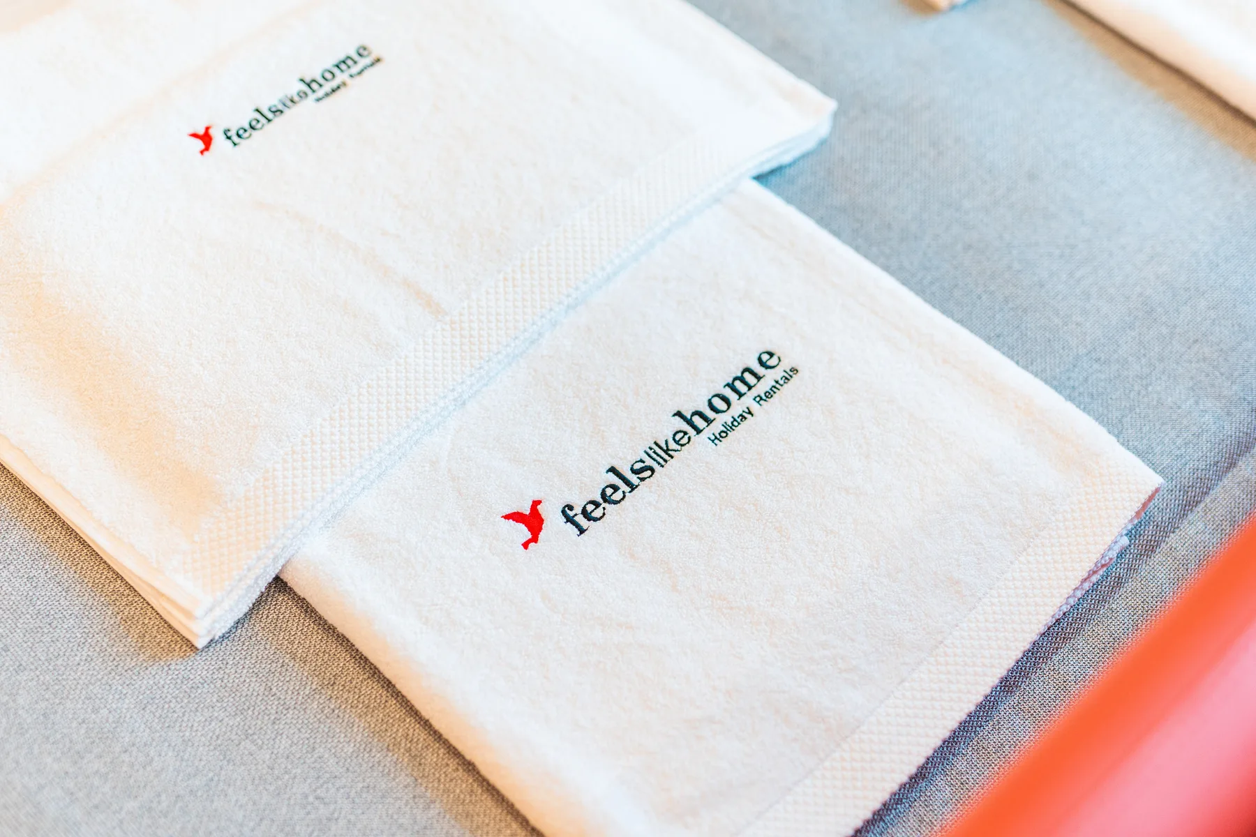 Two folded white towels with embroidered logos rest on a light surface.
