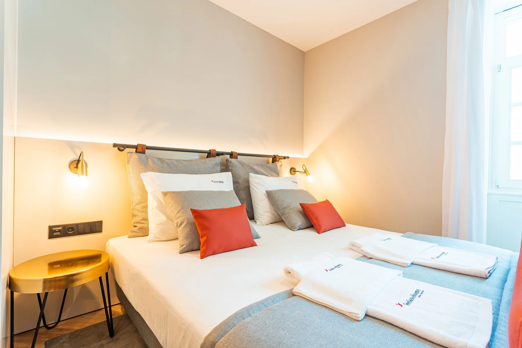 A bedroom with a neatly made bed and folded towels beside a window.