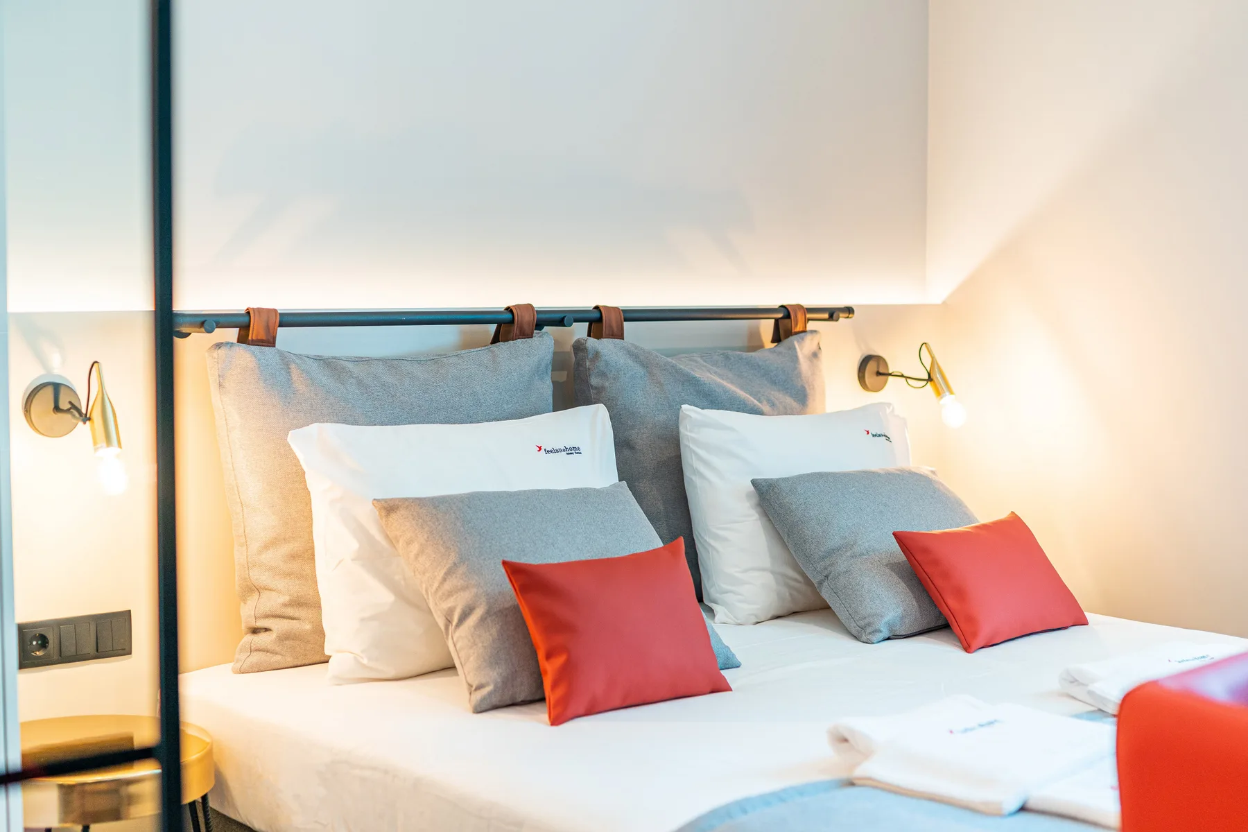 A bedroom with a bed dressed in white linens and red accent pillows.