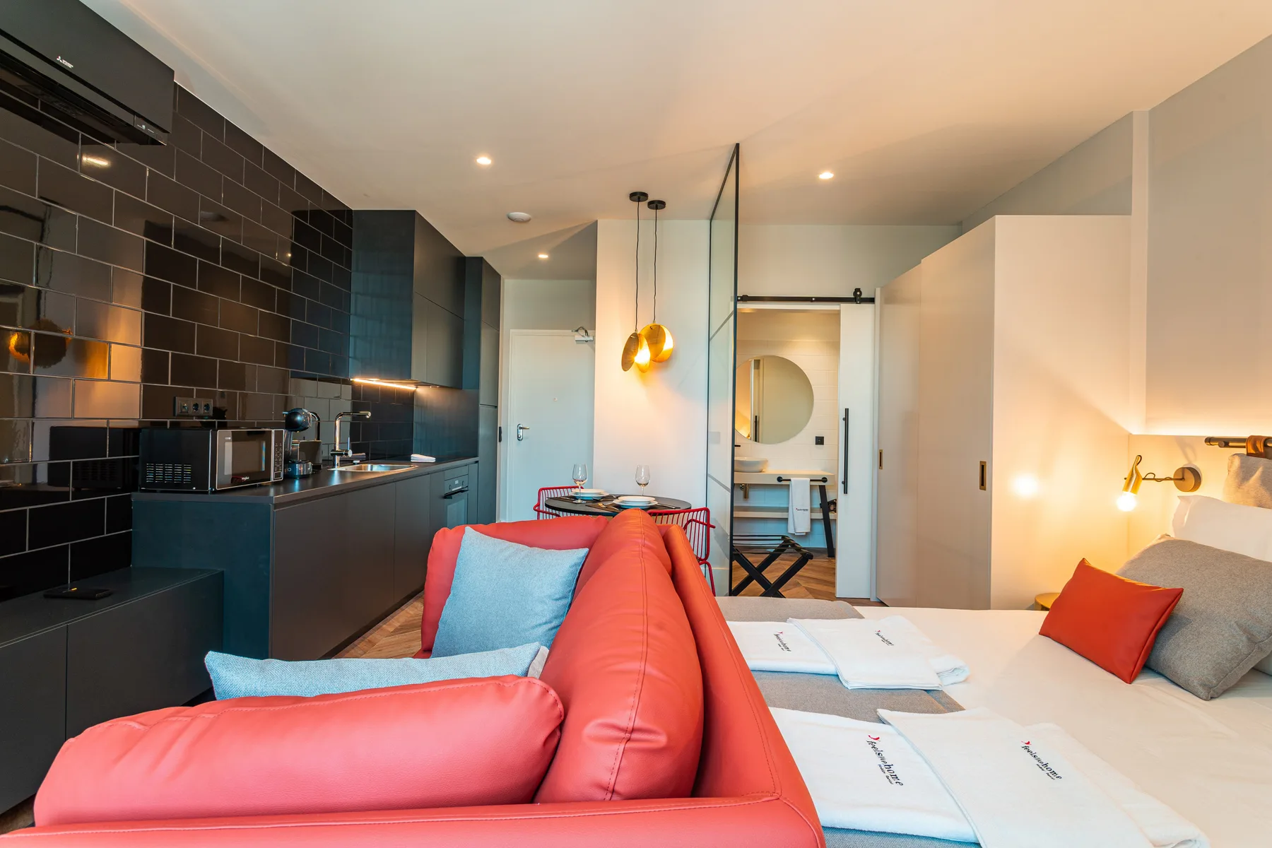 A studio interior combines a kitchenette, red seating, and beds.
