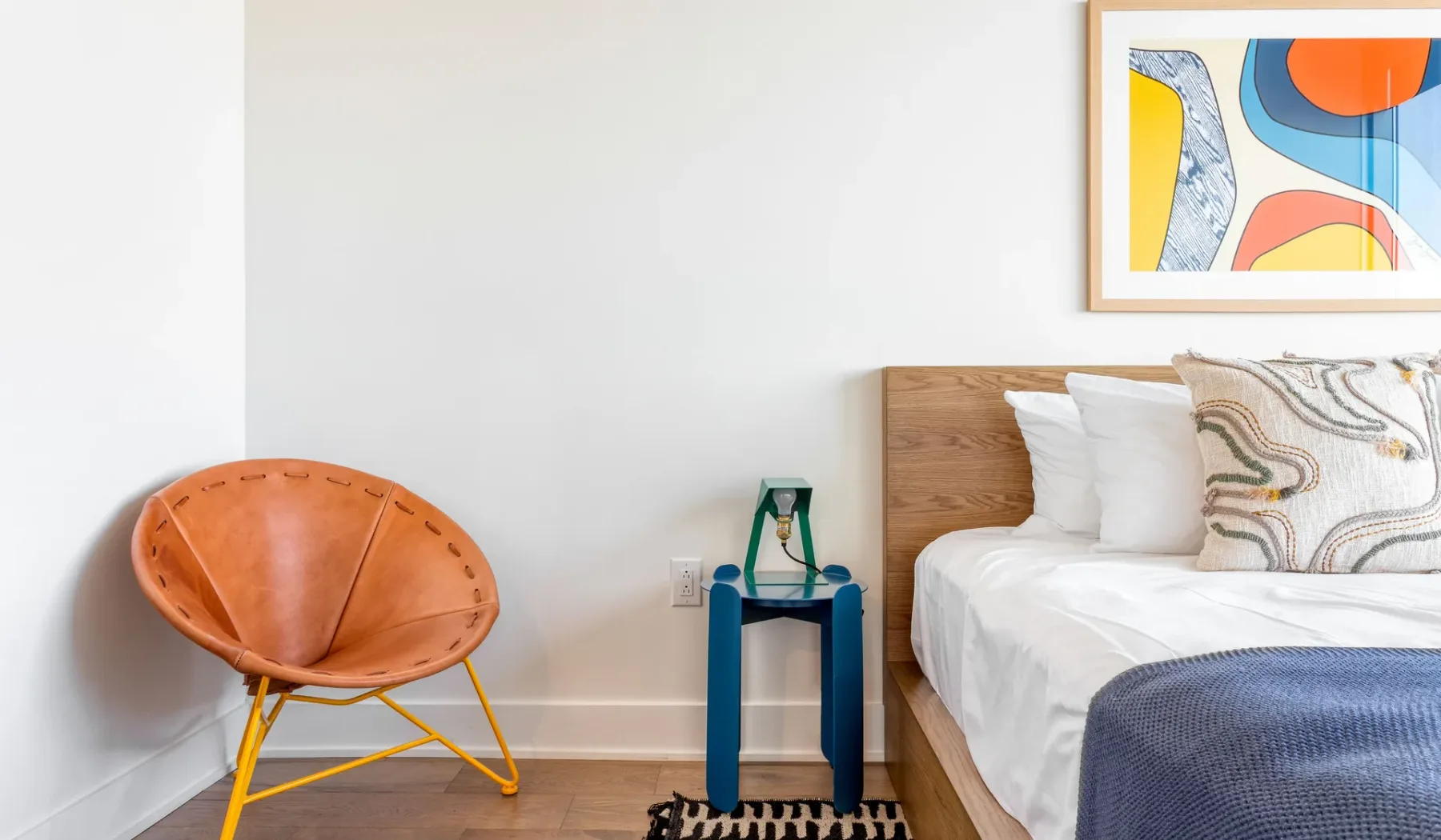 A bedroom with a bed and an orange accent chair beside it.