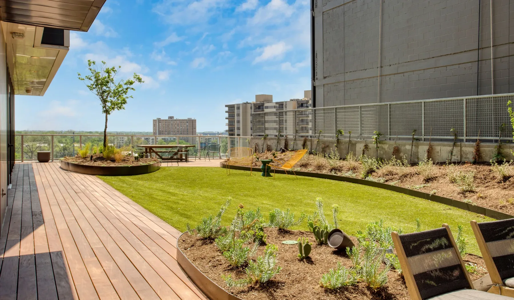 A landscaped rooftop garden features a lawn, raised flower beds, and wooden decking.