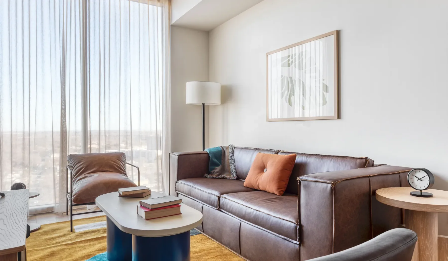 A living room with a leather sofa and tall curtained windows.