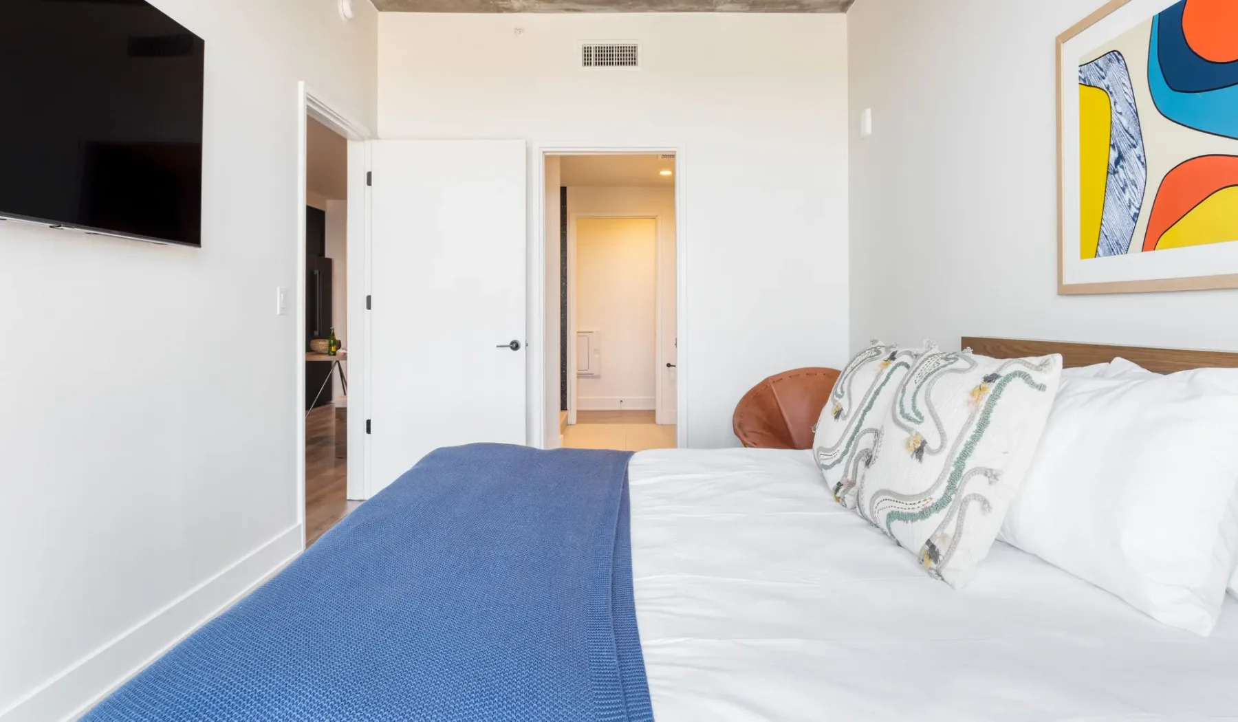 A bedroom with a bed, blue bedspread, and colorful wall art.