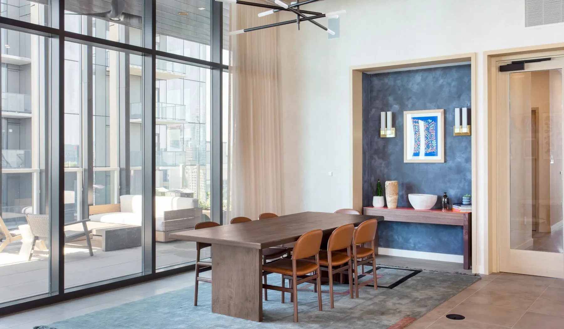 A dining area with a long table and chairs beside large windows.