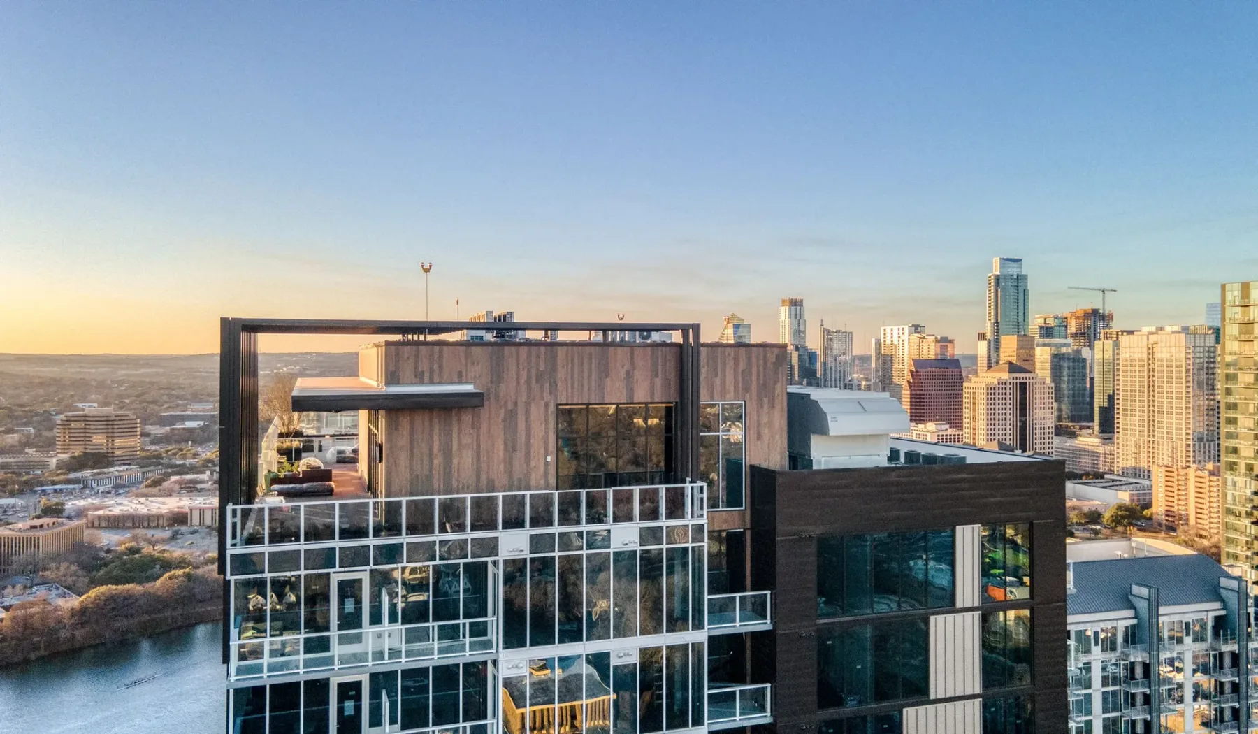 A modern high-rise building overlooks a city skyline at sunset.