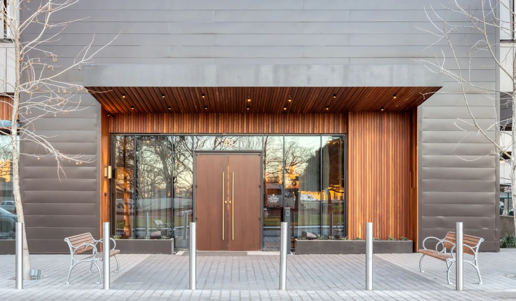 A modern building entrance with glass doors and benches on either side.