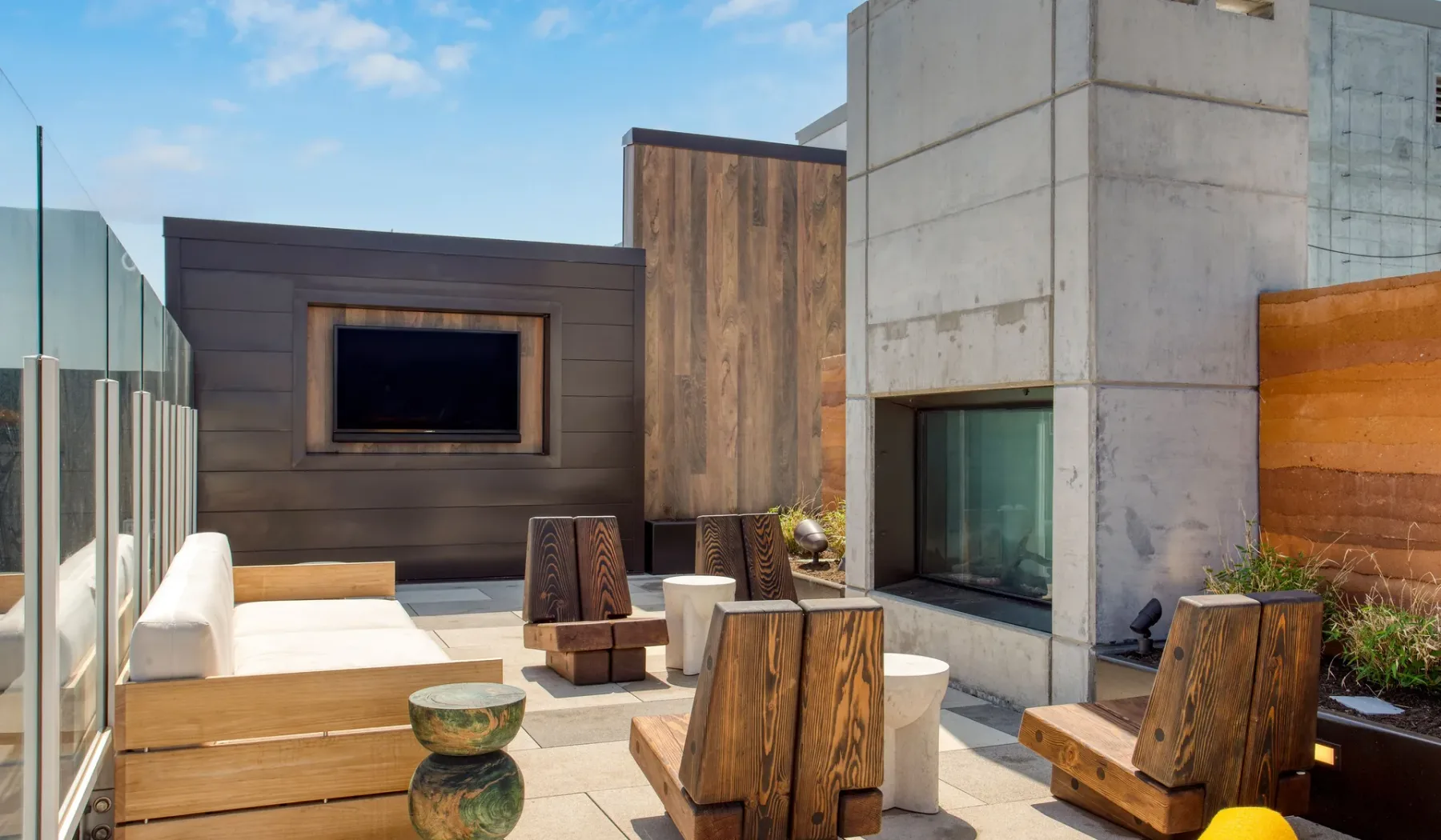 An outdoor patio has wooden seating around a low table beside a modern concrete wall.