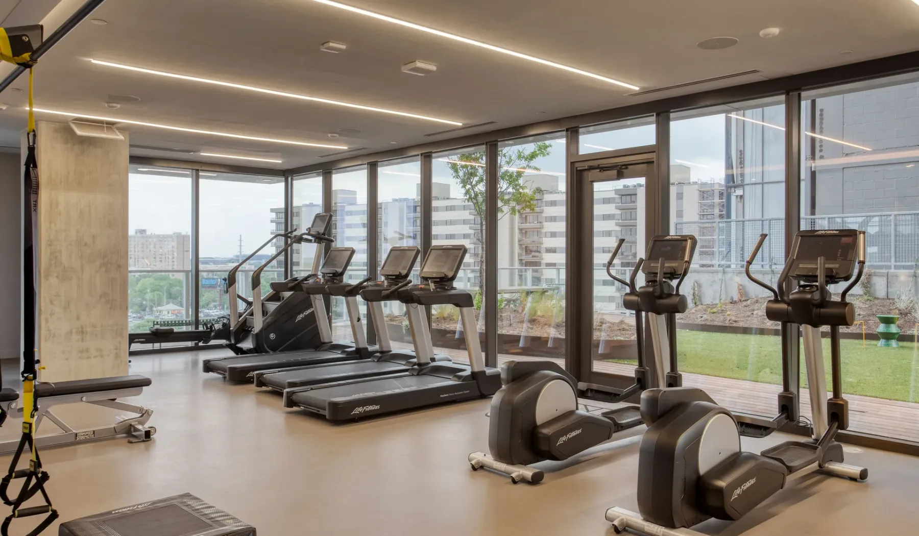 A gym with treadmills and exercise machines beside large windows.