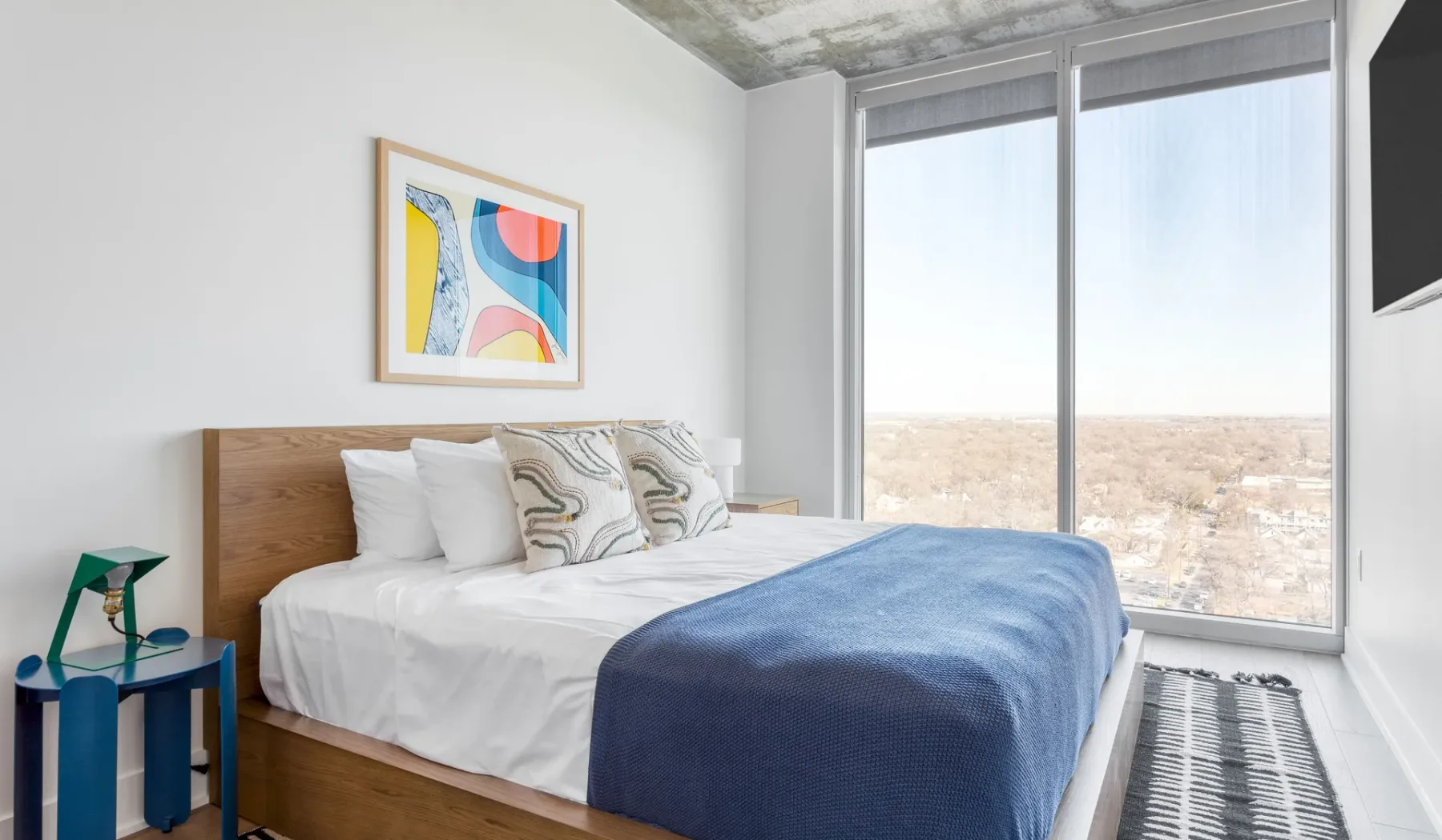 A bright bedroom with a neatly made bed and large windows overlooking the landscape.