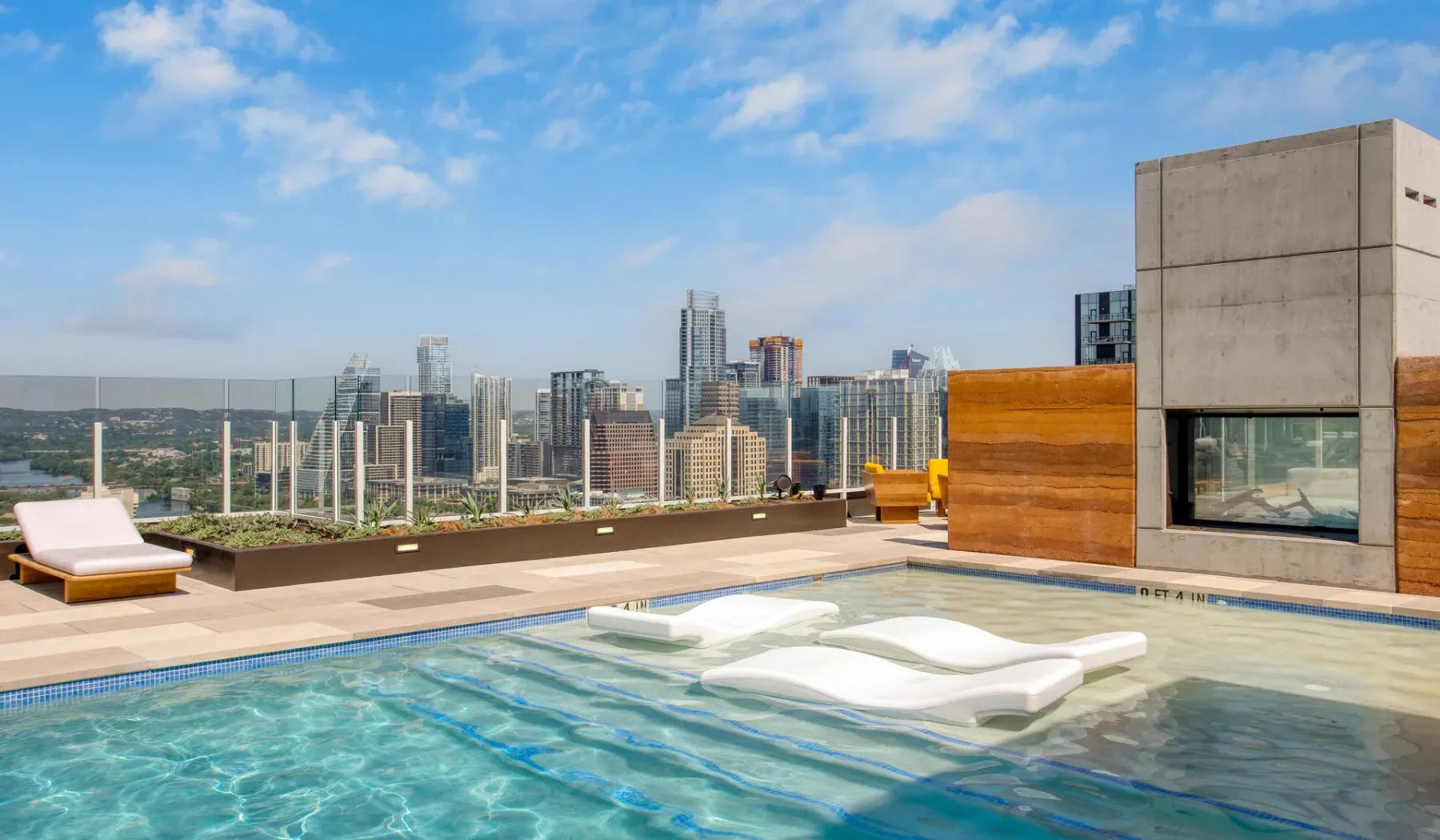 A rooftop pool overlooks a city skyline, with loungers beside the water.