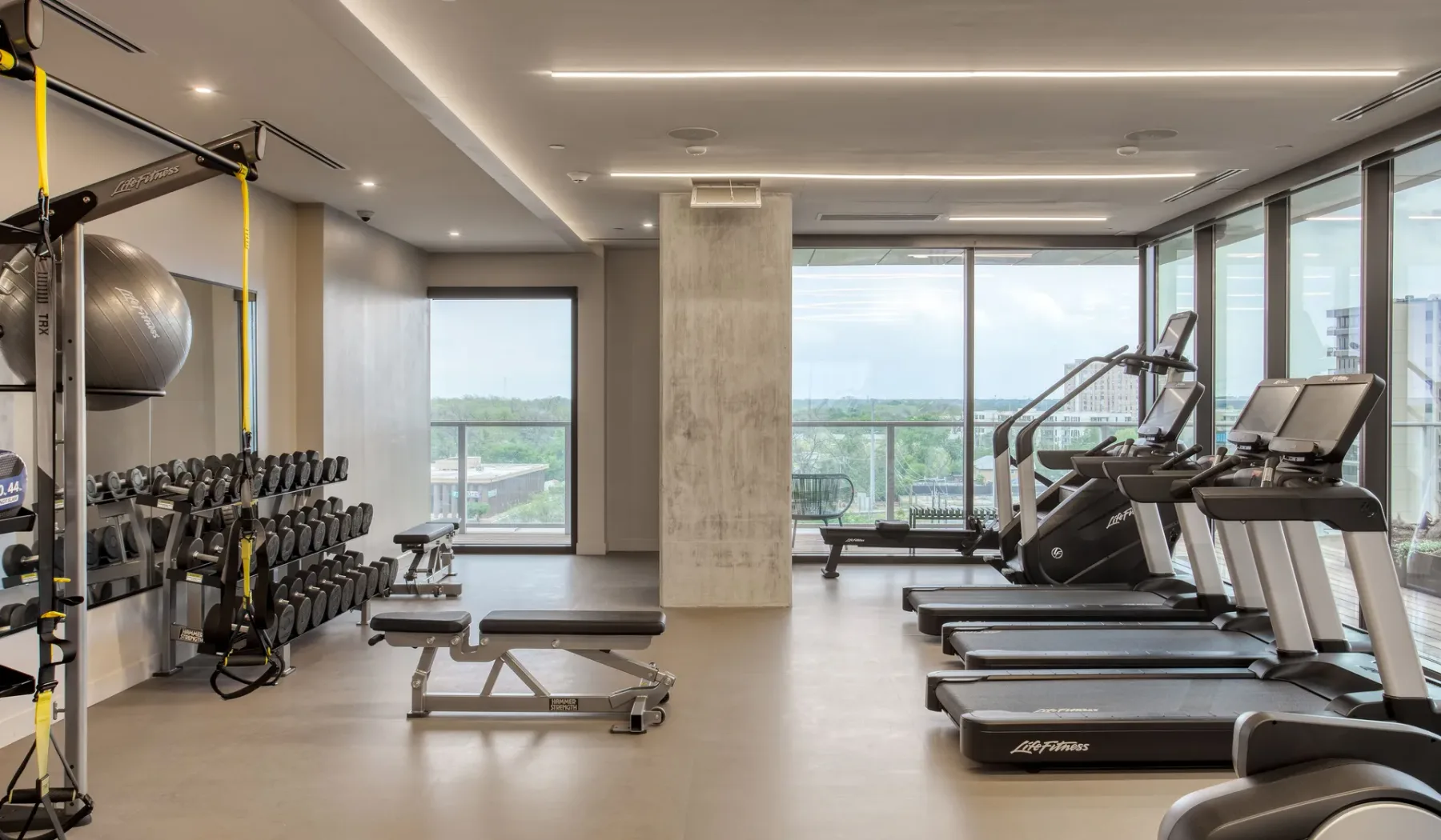A fitness room with treadmills, weight racks, and large windows.