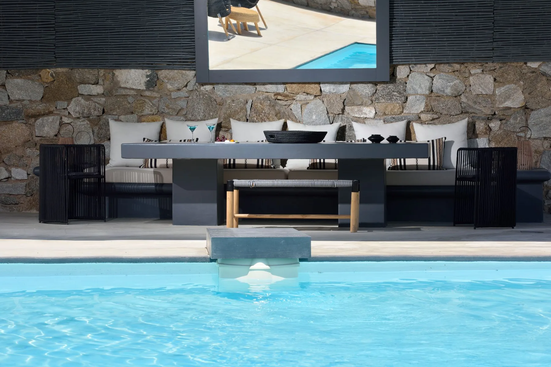 Outdoor seating area beside a swimming pool, with a dining table against a stone wall.